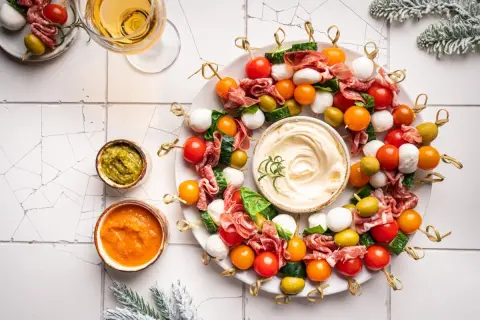 Kolorowe przystawki na zimno w kształcie wieńca, z mozzarellą, pomidorkami, oliwkami i salami, podane z dipami.