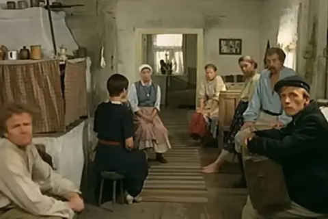 Scena z filmu "Znachor", gdzie nagrywali w wiejskiej chacie. Ludzie siedzą w skromnym wnętrzu, czekając na pomoc.
