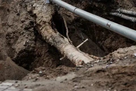 Gros plan sur un ancien tuyau en plomb dans une tranchée, à côté d'un nouveau tuyau gris. Travaux de rénovation dans une maison.