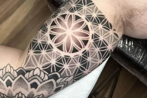 Ein Mann trägt ein geometrisches Tattoo am Oberarm. Das Muster erinnert an eine Blume des Lebens und ist fein gestochen.