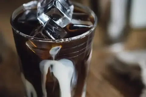 Ett glas iskaffe på snabbkaffe med mjölk som rinner ner längs glaset och isbitar som flyter i kaffet.