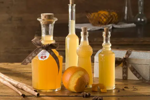 Flaschen mit selbstgemachtem Schnaps, Orangen, Zimtstangen und Sternanis auf Holztisch.