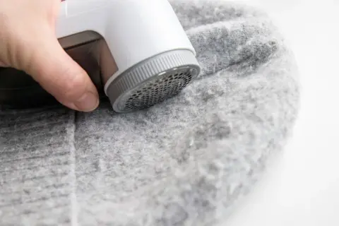 Ein Wollpullover, der eingelaufen ist, wird mit einem Fusselrasierer von Knötchen befreit.