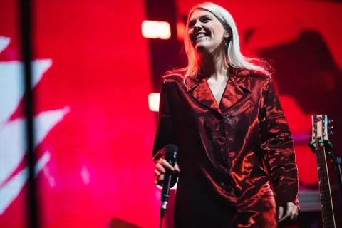 Uśmiechnięta dziewczyna pop w błyszczącej, czerwonej marynarce trzyma mikrofon na tle czerwonej sceny.