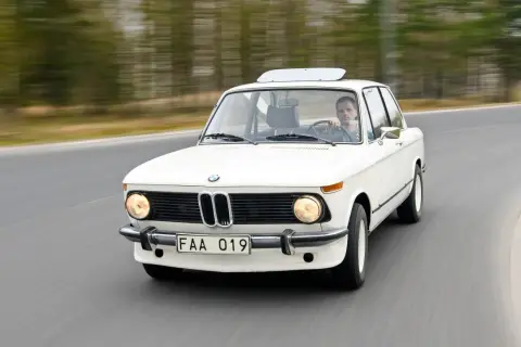 Vit BMW 70-talsklassiker kör på en väg, med en man bakom ratten.