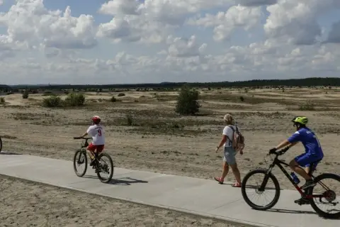 Ludzie na rowerach i pieszo na ścieżce rowerowej w krajobrazie pustynnym.