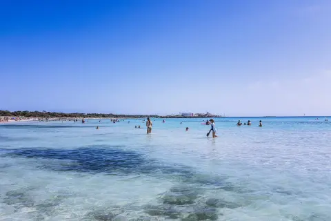 Słoneczny dzień na plaży Es Trenc. Ludzie kąpią się w krystalicznie czystej wodzie, ciesząc się wakacjami.
