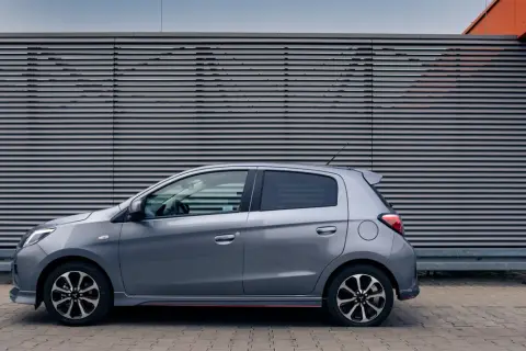 Szary Mitsubishi Space Star stoi na tle nowoczesnej, szarej ściany z poziomymi żaluzjami.