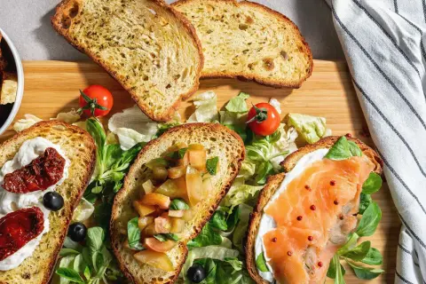 Bruschette senza pomodoro: fette di pane tostato con salmone, crema, pomodori secchi e verdure fresche.