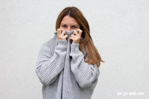 Frau versteckt sich hinter ihrem kuscheligen Pullover, der sich statisch aufgeladen anfühlt.