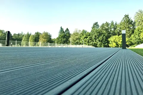 Szara deska kompozytowa tworzy nowoczesną nawierzchnię tarasu, otoczoną zielenią i jasnym niebem.