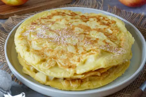 Ein Stapel goldbrauner Apfelpfannkuchen, bestäubt mit Puderzucker. Ein köstliches Apfelpfannkuchen Rezept für jeden Anlass.