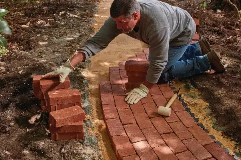 Man laying red bricks to create a new brick walkway in a garden.