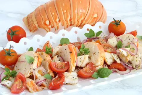 Aragosta alla catalana, un piatto fresco con code di aragosta, pomodorini, cipolla rossa e basilico, guarnito con una coda intera.