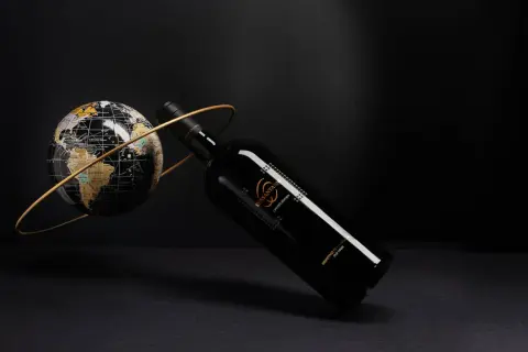 Elegancka butelka Sessantanni Primitivo di Manduria, otoczona złotym pierścieniem, obok globusa.