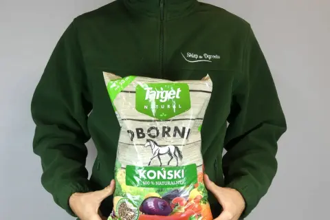 Osoba w zielonej bluzie trzyma worek z napisem "Obornik koński granulowany". Produkt jest naturalny i przeznaczony do ogrodu.