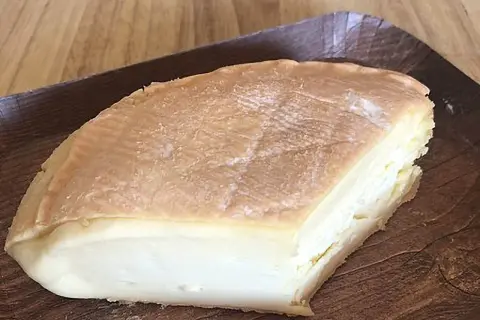 Un morceau de fromage à pâte molle, à la croûte orangée et à l'odeur prononcée, servi sur un plateau en bois.