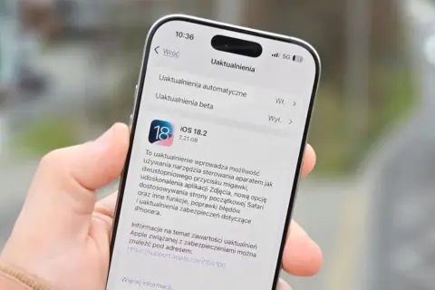 Dłoń trzyma iPhone'a z otwartym ekranem aktualizacji iOS 18.2.
