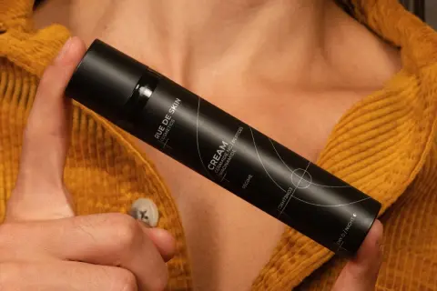 Dłoń trzyma czarny flakon kremu z napisem "Niacynamid". Czy wybrać retinol czy niacynamid?