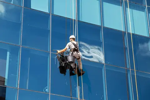 Trabajador en arnés limpiando cristales altos de un edificio moderno.