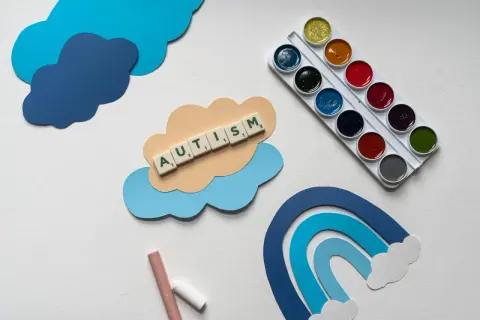 Terapia dziecka z aspergerem w domu: chmurki, tęcza, kredki i farby. Słowo AUTISM ułożone z liter.