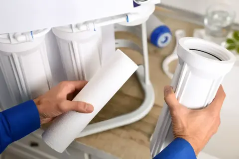 Main tenant d'un filtre, un homme prépare l'entretien de son osmoseur.