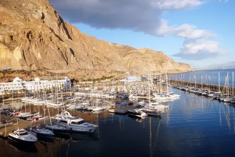 El puerto deportivo Aguadulce, con sus barcos amarrados y un hotel blanco, se extiende bajo una imponente montaña rocosa.