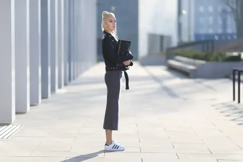 Elegancka kobieta w skórzanej kurtce i ołówkowej spódnicy, prezentująca stylowe adidas superstar stylizacje.