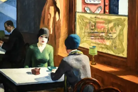 A woman in a green dress and black hat sits at a table, a small teapot before her. Hopper's "Chop Suey" captures a moment of quiet contemplation.