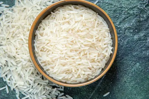 Chicchi di riso basmati in una ciotola e sparsi su una superficie scura. Scopri le proprietà del riso basmati.