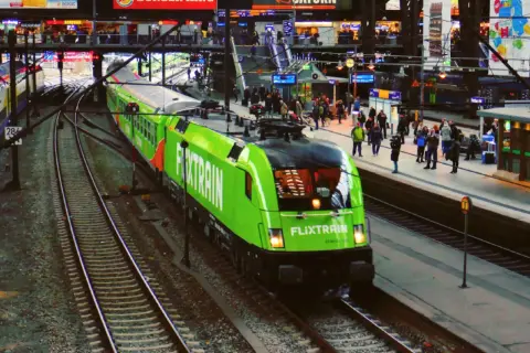 Ein grüner FlixTrain fährt in Berlin Hbf ein. Reisende warten auf dem Bahnsteig.