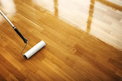 Rodillo aplicando barniz para limpiar suelo madera. El brillo refleja la luz.