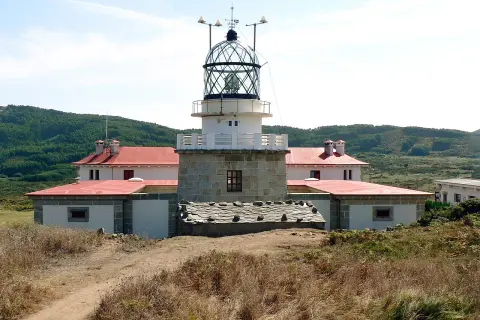 El faro de estaca de bares se alza imponente sobre la costa, con sus edificios blancos y tejados rojos rodeados de vegetación.