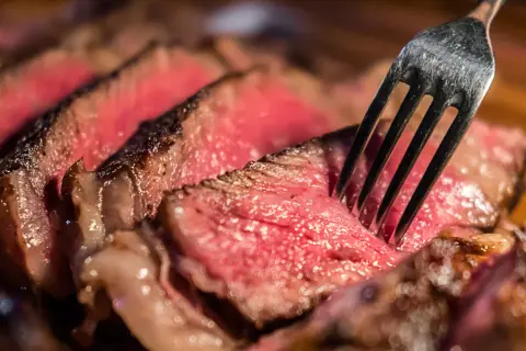 Soczysty stek, idealny na dietę lwa. Widelec wbity w krwisty kawałek mięsa.