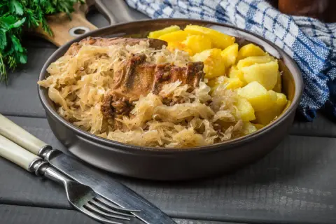 Pyszne żeberka w kapuście z ziemniakami, podane w misie. Obok sztućce i serwetka.