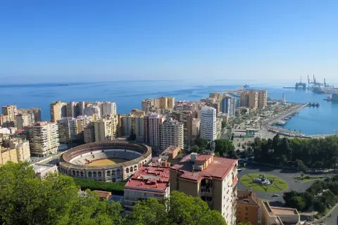 Vista panorámica desde el mirador de Gibralfaro: la plaza de toros, el puerto y la ciudad de Málaga bajo un cielo azul.