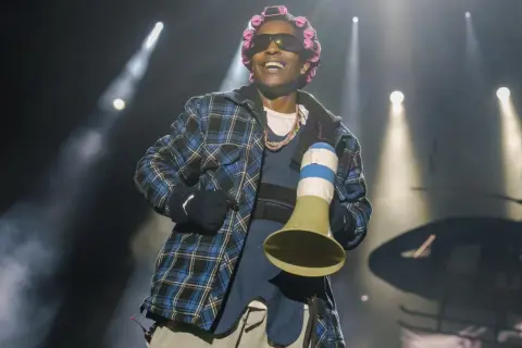 Raper A$AP Rocky, z wałkami na włosach i w kratowanej koszuli, śmieje się na scenie. Czy asap rocky żyje? Tak, i to w świetnej formie!