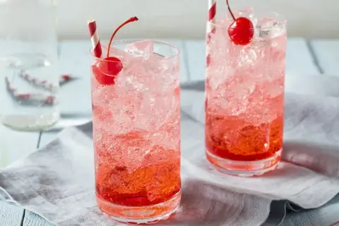Erfrischende Crodino Rezepte: Zwei Gläser mit Eis, Kirschen und roten Strohhalmen.