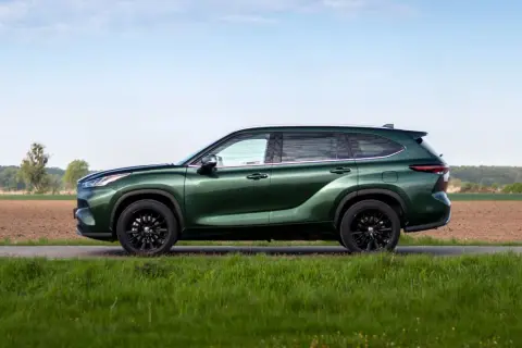 Zielony Toyota Highlander z czarnymi felgami stoi na tle pól i nieba.
