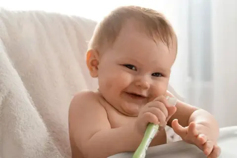 Uśmiechnięte dziecko bawi się swoją pierwszą szczoteczką do zębów.