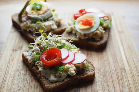 Pyszna pasta jajeczna z makrelą na ciemnym pieczywie, udekorowana kiełkami, rzodkiewką i papryką. Idealna na szybkie śniadanie.