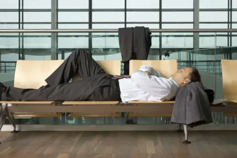 Biznesmen śpi na ławce w poczekalni lotniska, próbując pokonać jet lag. Ile trwa jet lag?