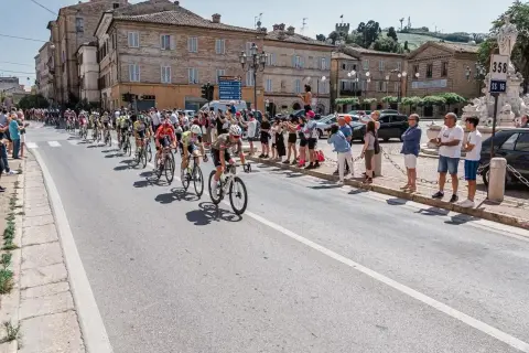 Ciclisti in gara durante il Giro d'Italia Marche, acclamati da spettatori festanti lungo la strada.