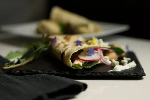 Ein gefüllter Wrap, der zeigt, was sind Tortillas: dünne Fladenbrote, gefüllt mit Hühnchen, Radieschen, Zwiebeln, Käse und Kräutern.