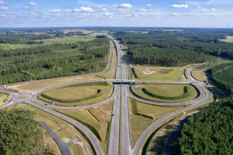 Nowa droga ekspresowa, idealna trasa do Kołobrzegu, przecina lasy i pola. W oddali widać farmę wiatrową.