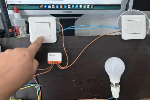 Installation d'un interrupteur zigbee va et vient. Un doigt actionne un interrupteur connecté à un module Sonoff, pilotant une ampoule.