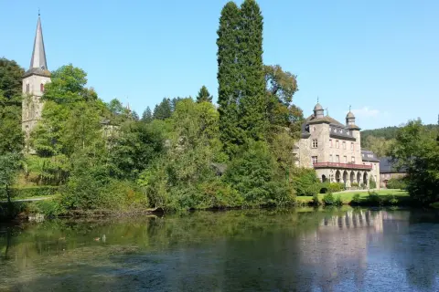 Schloss und Kirche in Wiehl Gummersbach, umgeben von üppigem Grün und einem ruhigen See.