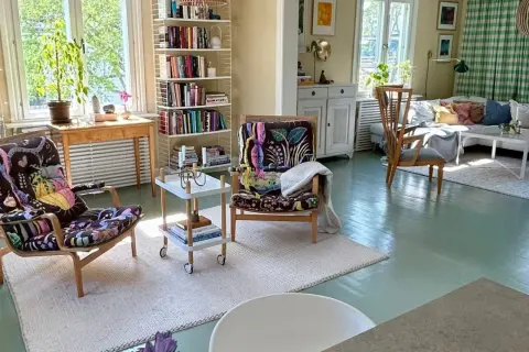 En inredd bokhylla med böcker och prydnadssaker. En fåtölj med färgglatt mönster står framför.