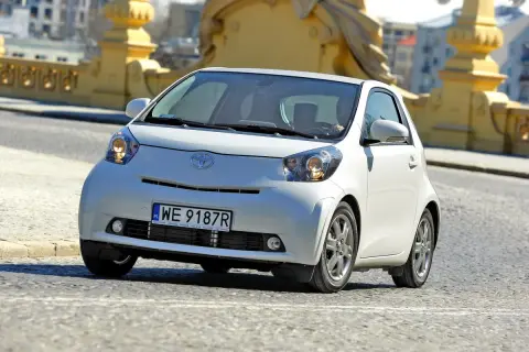 Biały, kompaktowy samochód Toyota iQ z polskimi tablicami WE 9187R jedzie po moście. Ten model, choć nie jest Daihatsu, oferuje podobną zwinność w mieście.