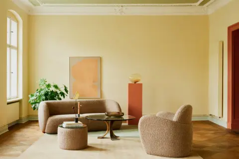 Ein Wohnzimmer mit gelben Wänden und einer grünen Decke, die frisch gestrichen wurde. Gemütliche Bouclé-Möbel laden zum Entspannen ein.